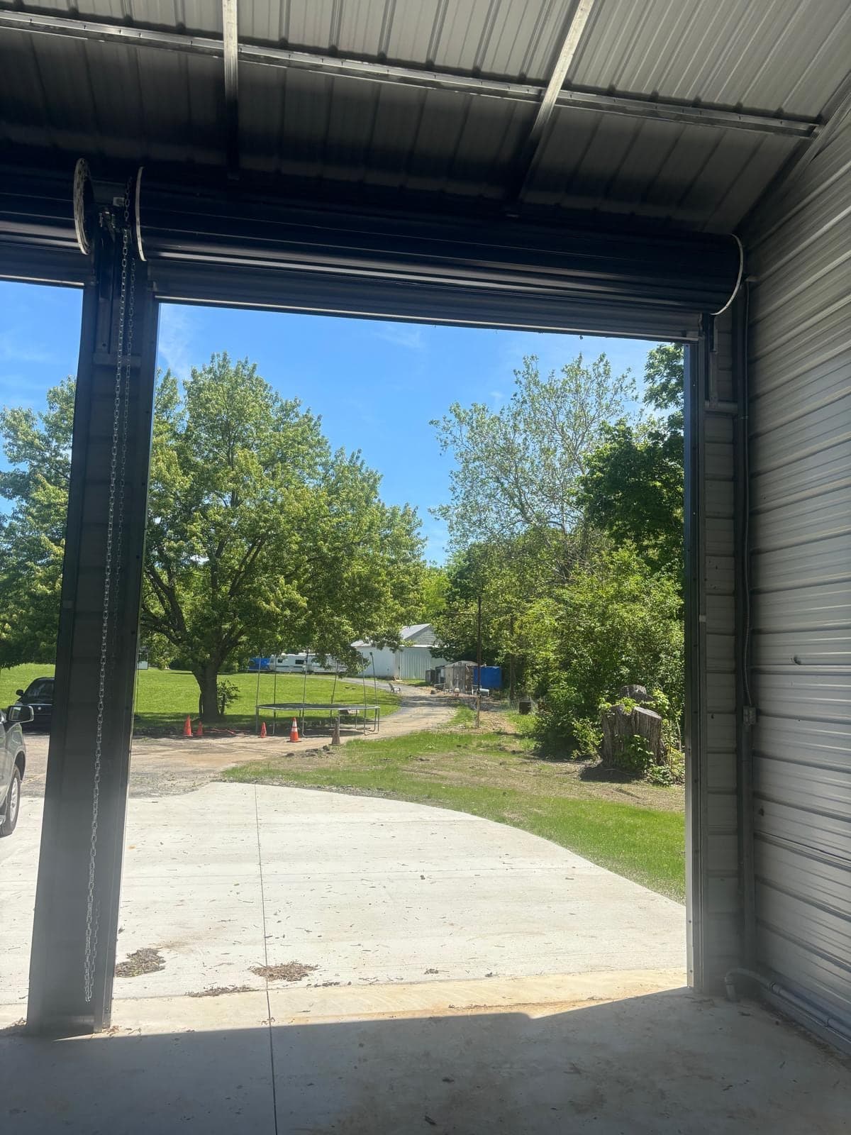 An open commercial bay door framing a view of a gravel drive, trees and a bright sky outside