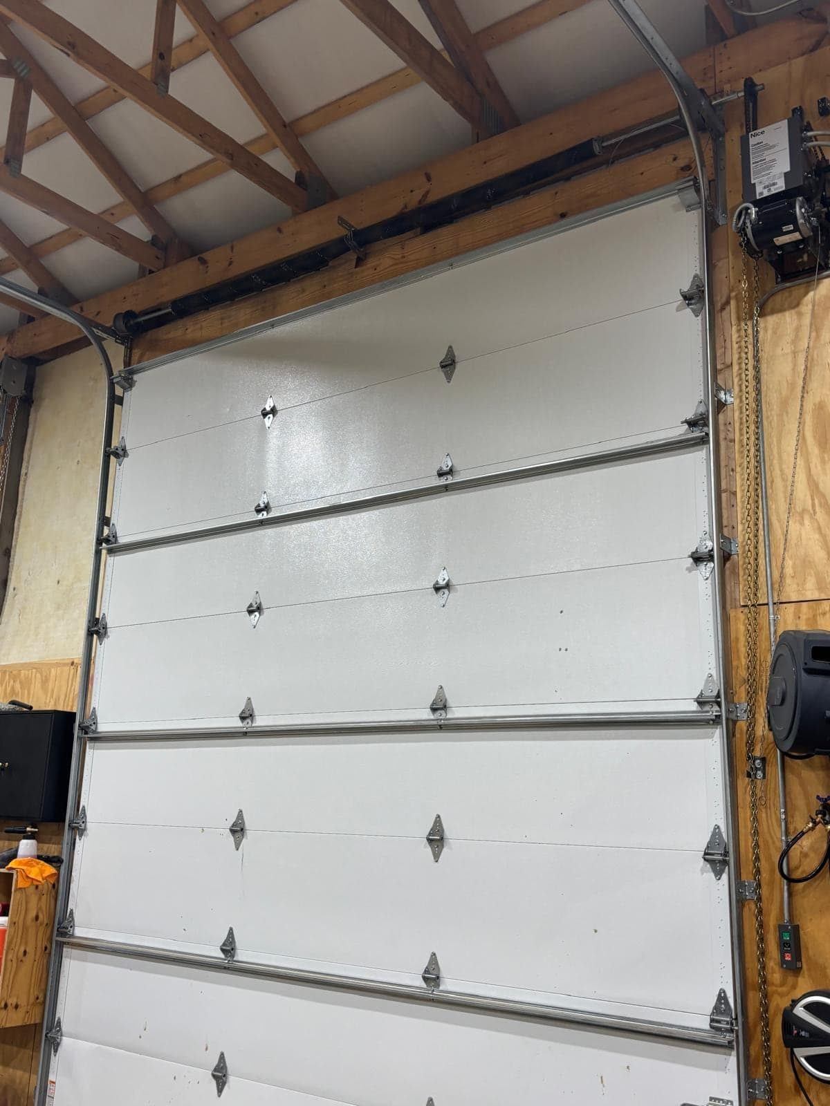 A tall white sectional door inside a pole barn, with the track and wooden posts visible