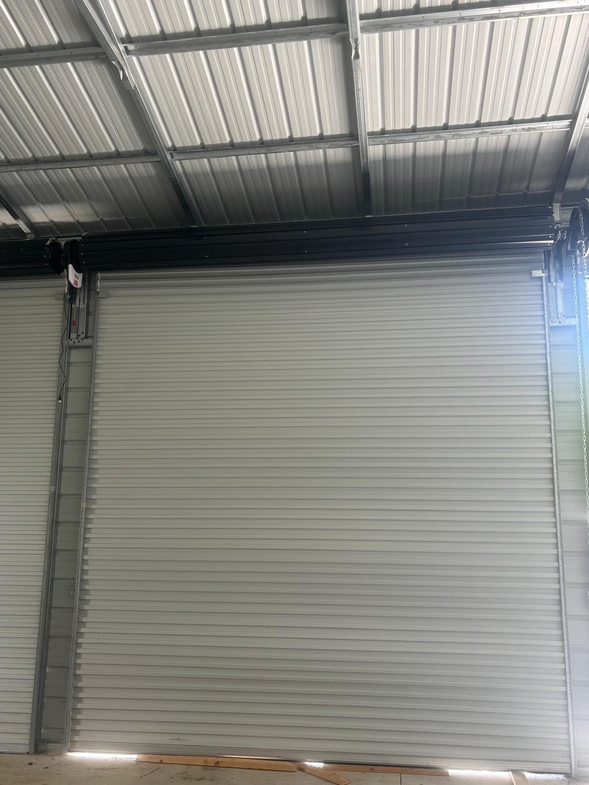 A grey rolling steel door inside a steel-framed commercial building, with the roof purlins overhead