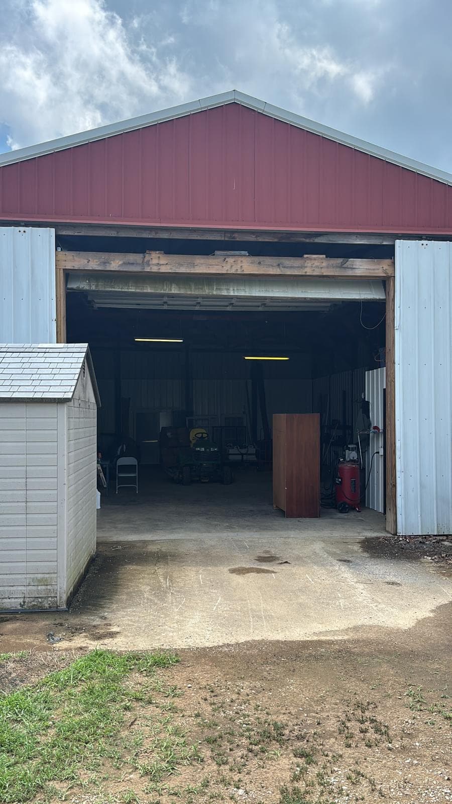 An open bay door on a commercial shop building with equipment, shelving and a small storage shed visible inside