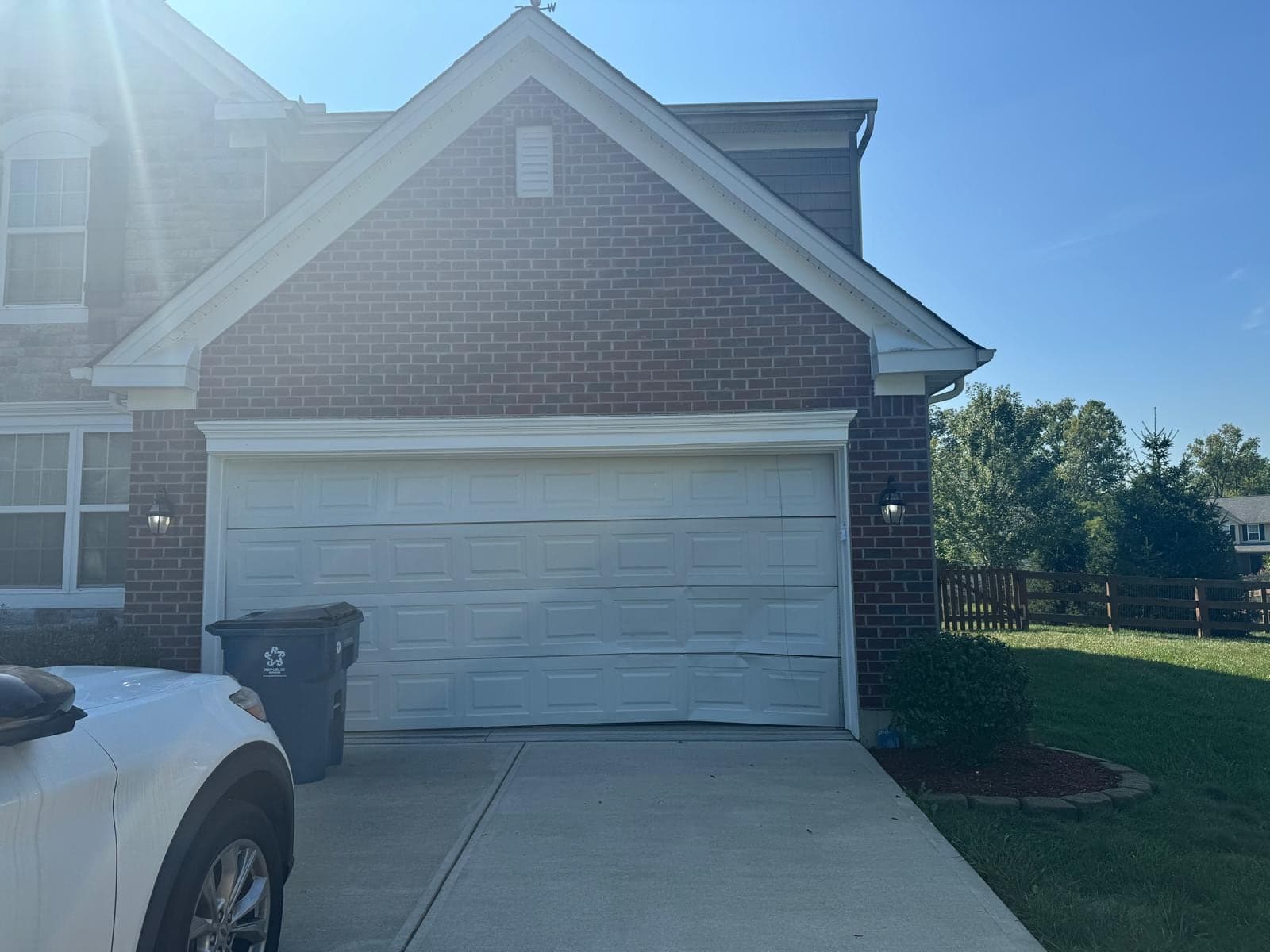 A new white raised-panel double garage door on a brick two-storey home with a steep gable above, photographed from the driveway