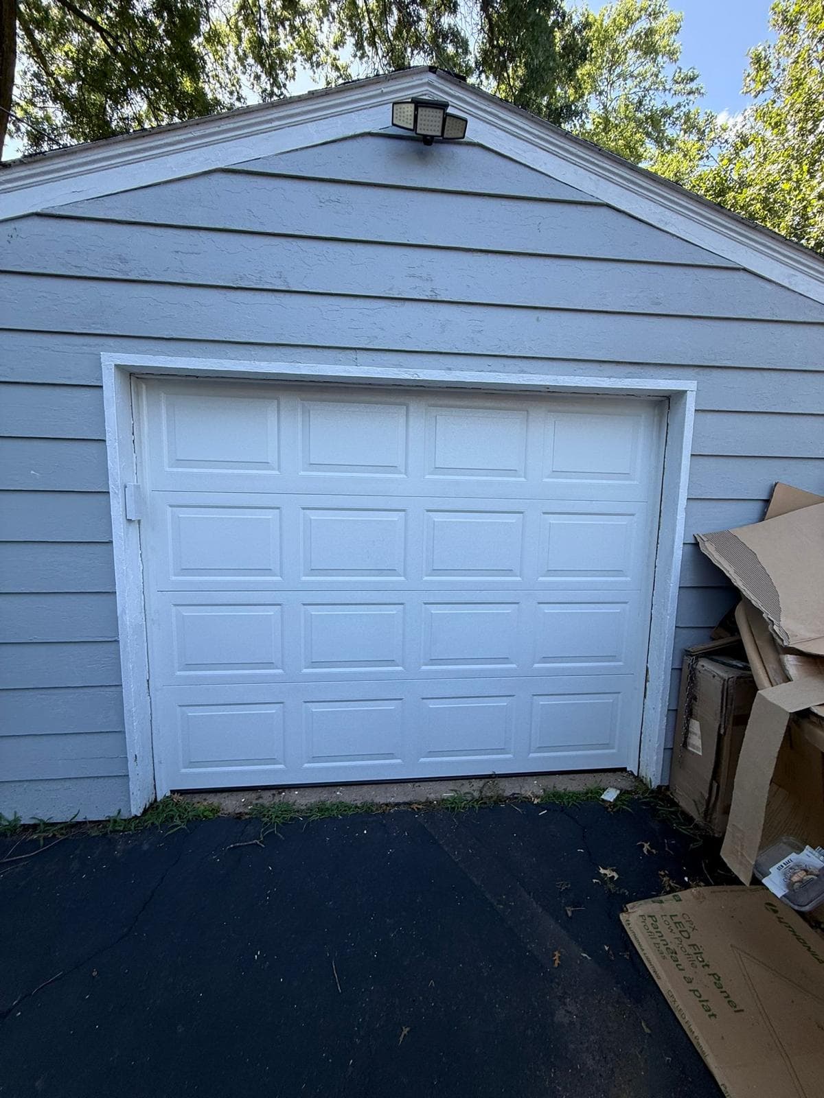 A newly installed white raised-panel steel garage door on a detached single-car garage with light blue siding, photographed from the driveway