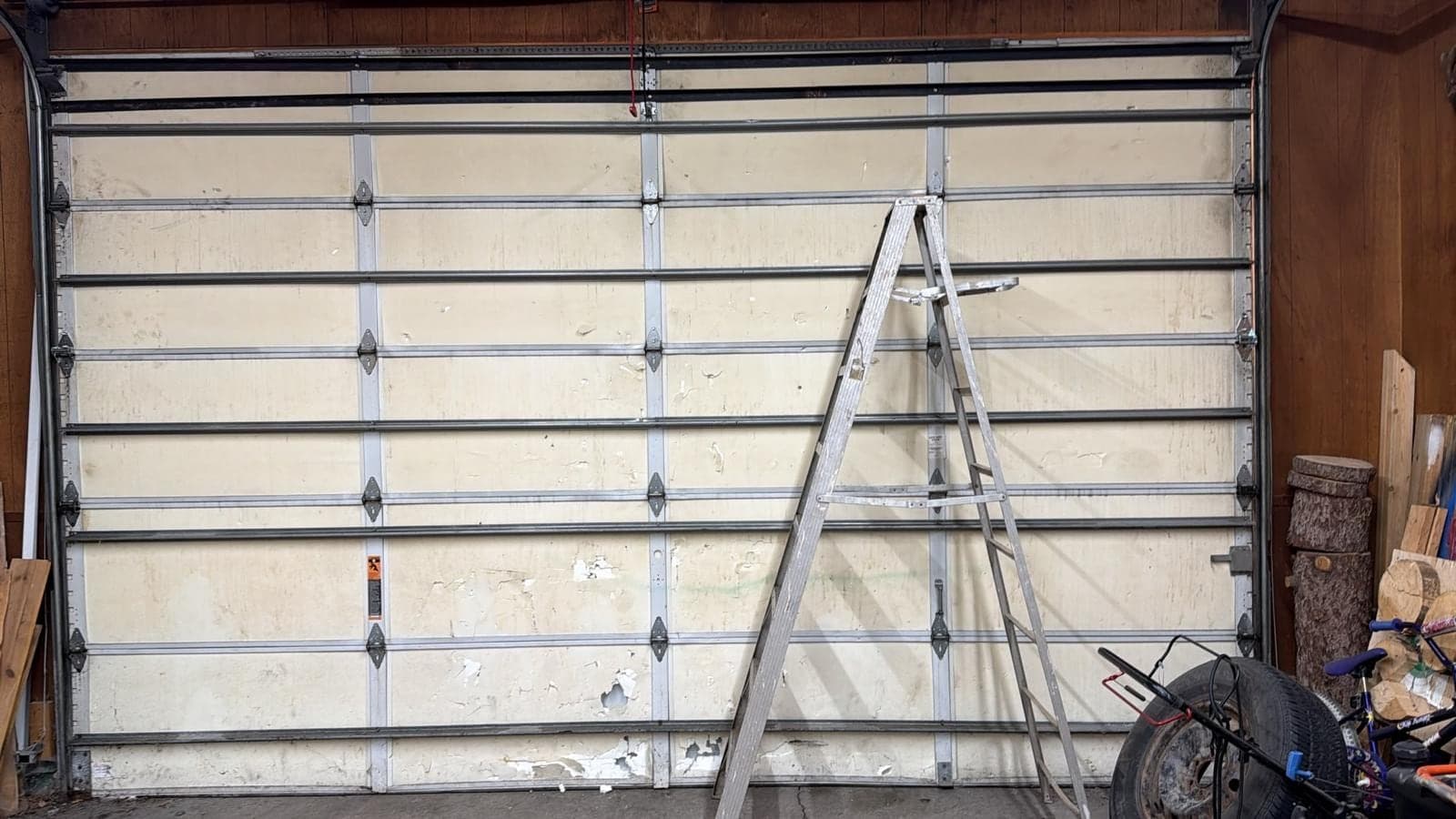 New white door sections stacked against the inside of an opening with a tall ladder leaning on them and the vertical tracks already in place