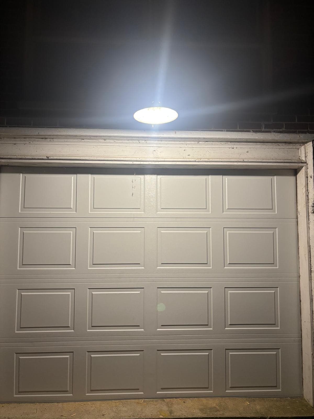 A new grey raised-panel garage door photographed at night under the garage light