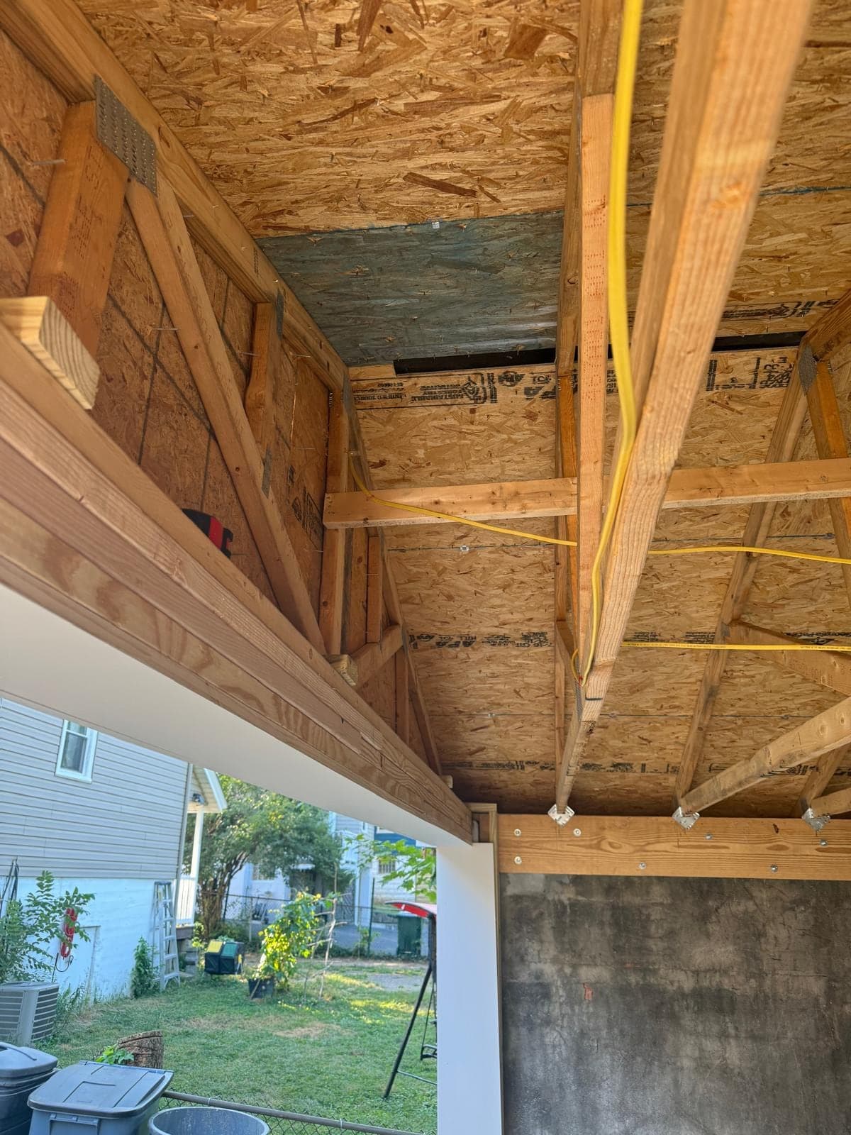 New timber header and framing above a garage opening seen from inside, with a yellow cable running through it and a neighbouring house visible outside