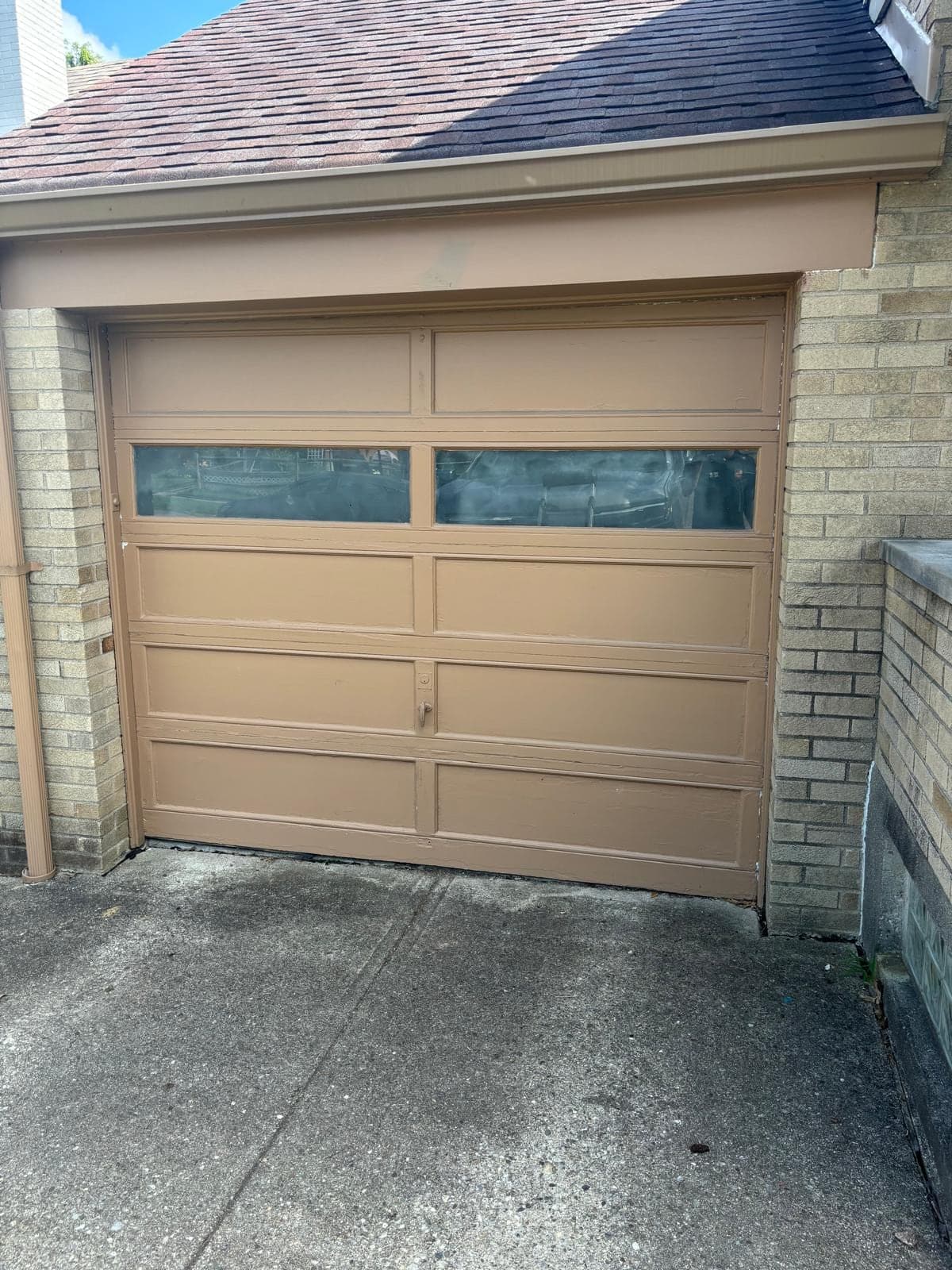 A new tan flush-panel single garage door with a row of narrow windows in the top section, set in a cream-coloured brick wall