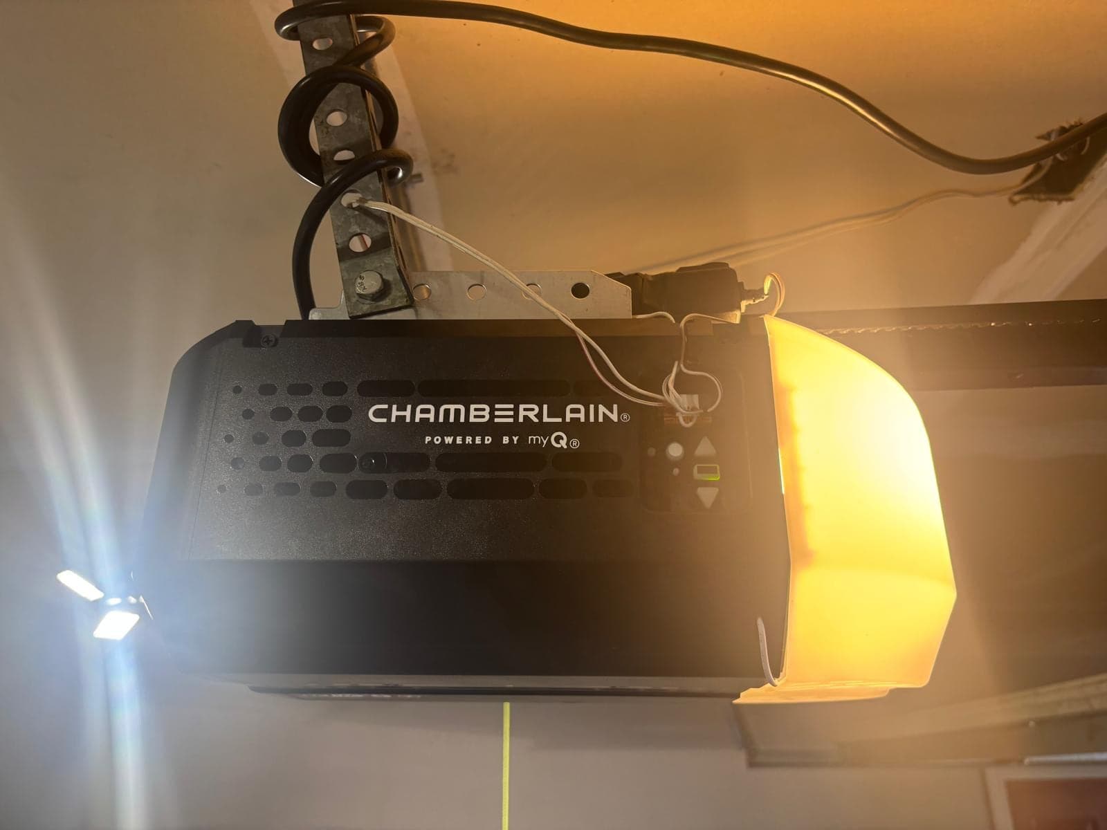 A Chamberlain myQ garage door opener mounted to the ceiling with its light on, photographed from below at installation