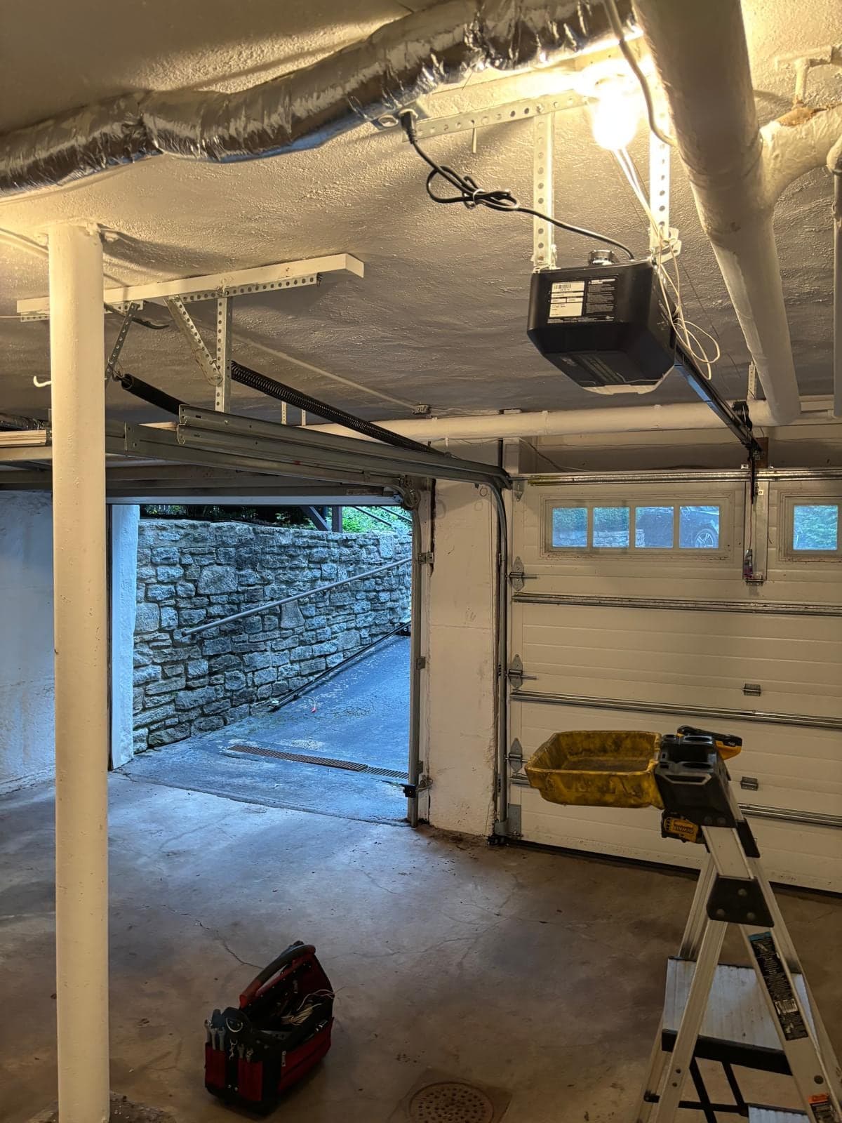 The same garage from the other side, with the new opener and rail overhead and the open door framing a stone retaining wall outside