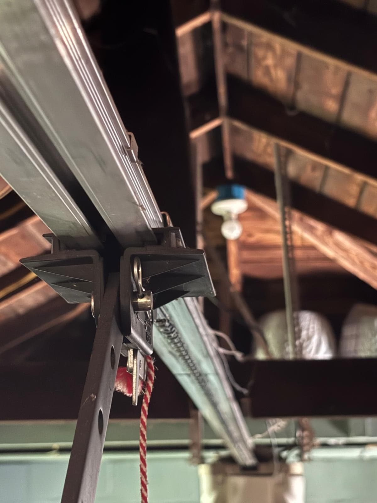 Close-up of an opener trolley and chain on the rail inside an older garage, with a bare bulb and rough timber overhead