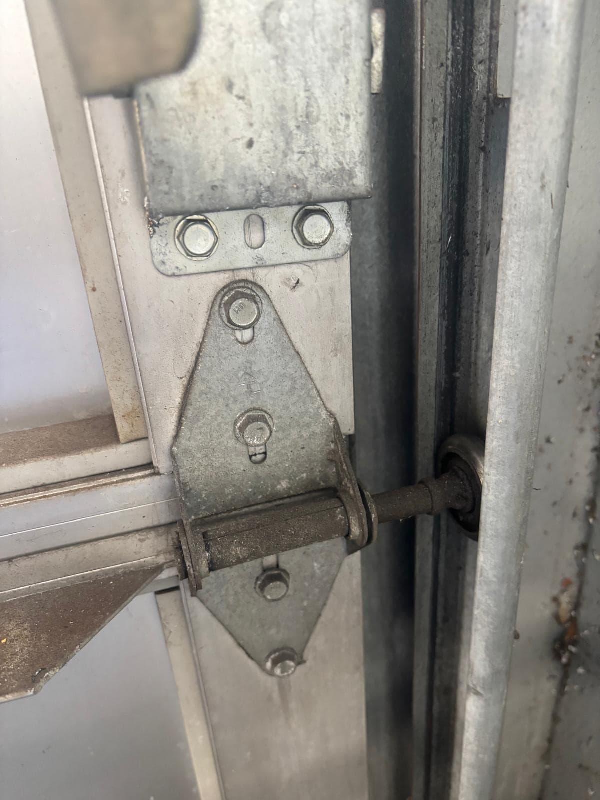 Close-up of a galvanised hinge and roller stem where a door section meets the vertical track, with some surface rust on the hardware