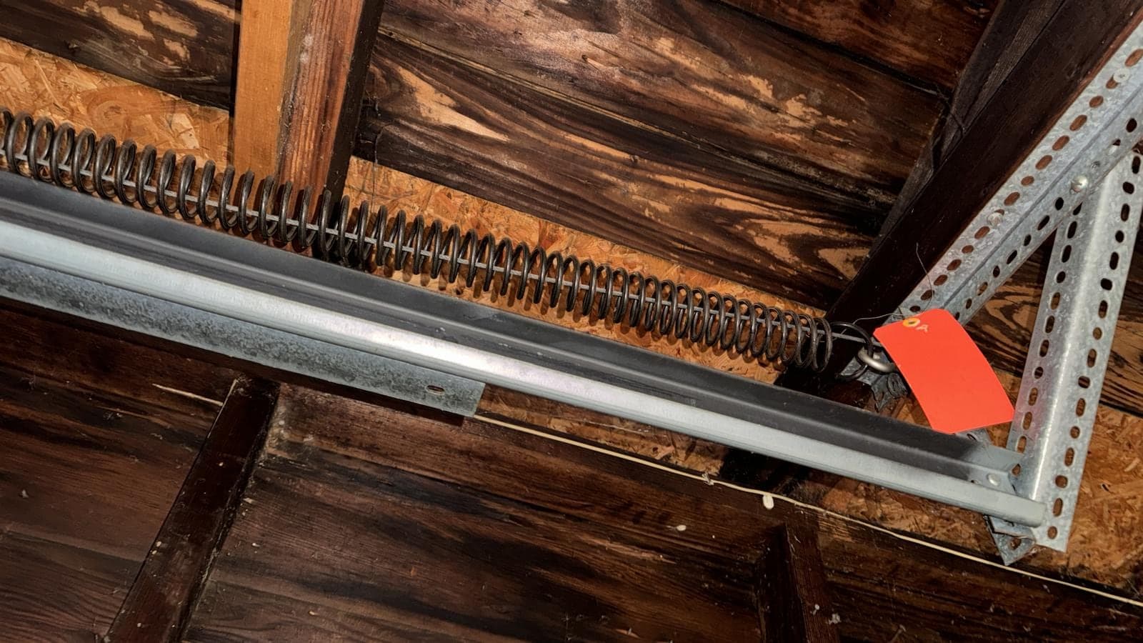An extension spring and its pulley running along a horizontal track under the exposed, darkened wood ceiling of an older garage