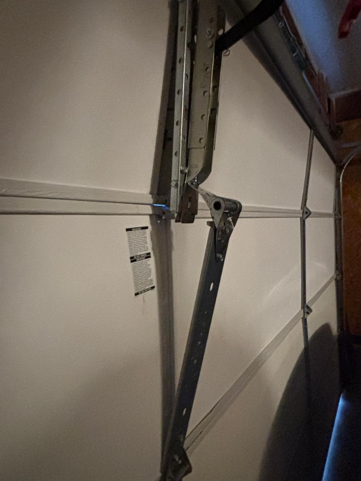 Close-up of a bent horizontal track and reinforcing strut inside a garage, with the white door sections behind them