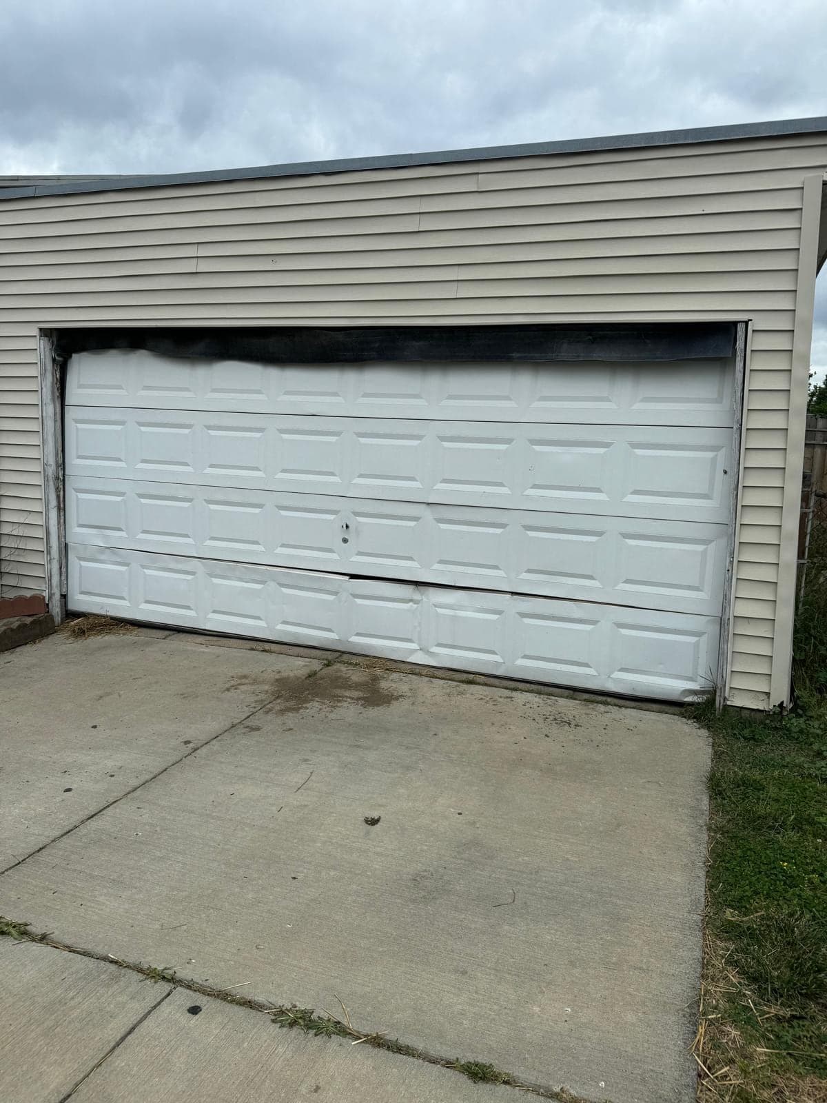 A white double garage door on a detached garage sitting crooked in its opening, with the right side lower than the left and the top section pulled out of line